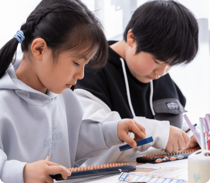 グレーの服で三つ編みをしている少女と短髪の少年が勉強している姿の写真